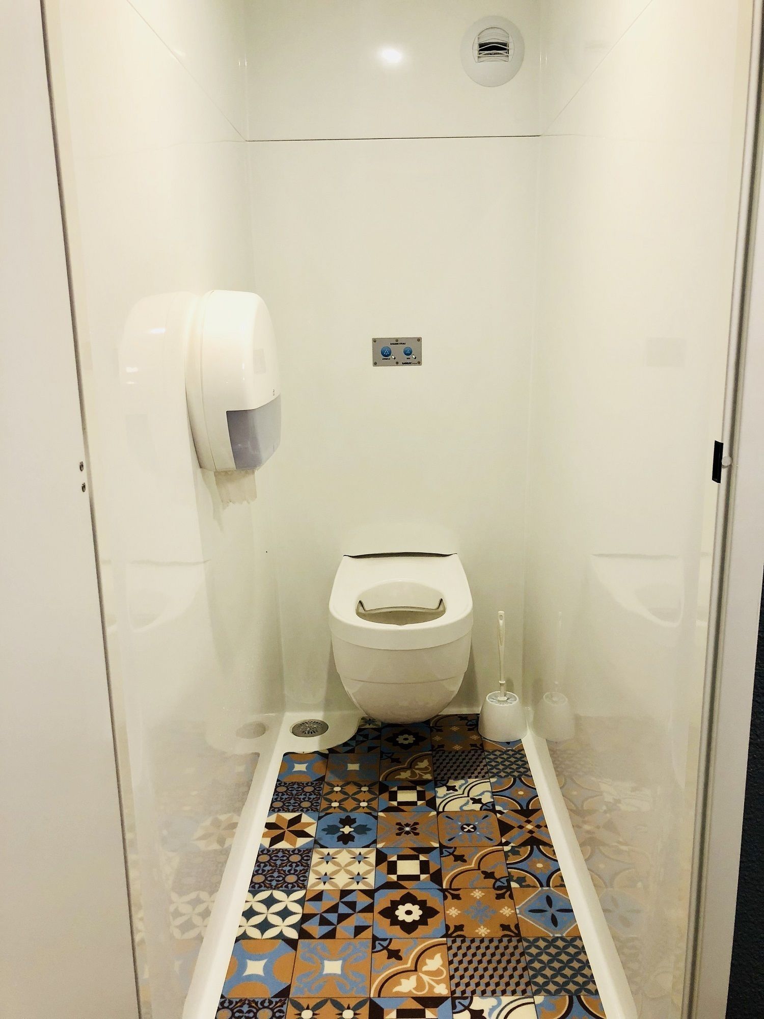 Une petite salle de bain fermée, équipée de toilettes, d’un sèche-mains et d’un bouton de chasse d’eau.