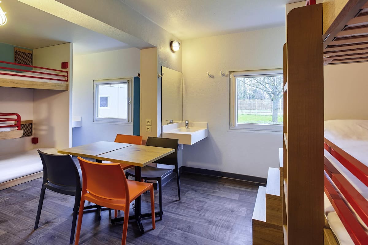 Ein Zimmer mit Etagenbetten, einem Tisch mit Stühlen, einem Waschbecken und einem Fenster.
