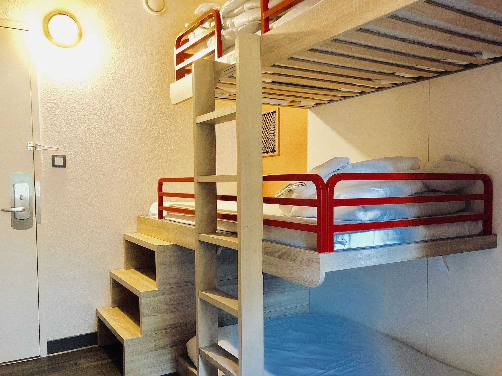 A bunk bed room with a wooden ladder, a door with a handle, and a light fixture on the wall.