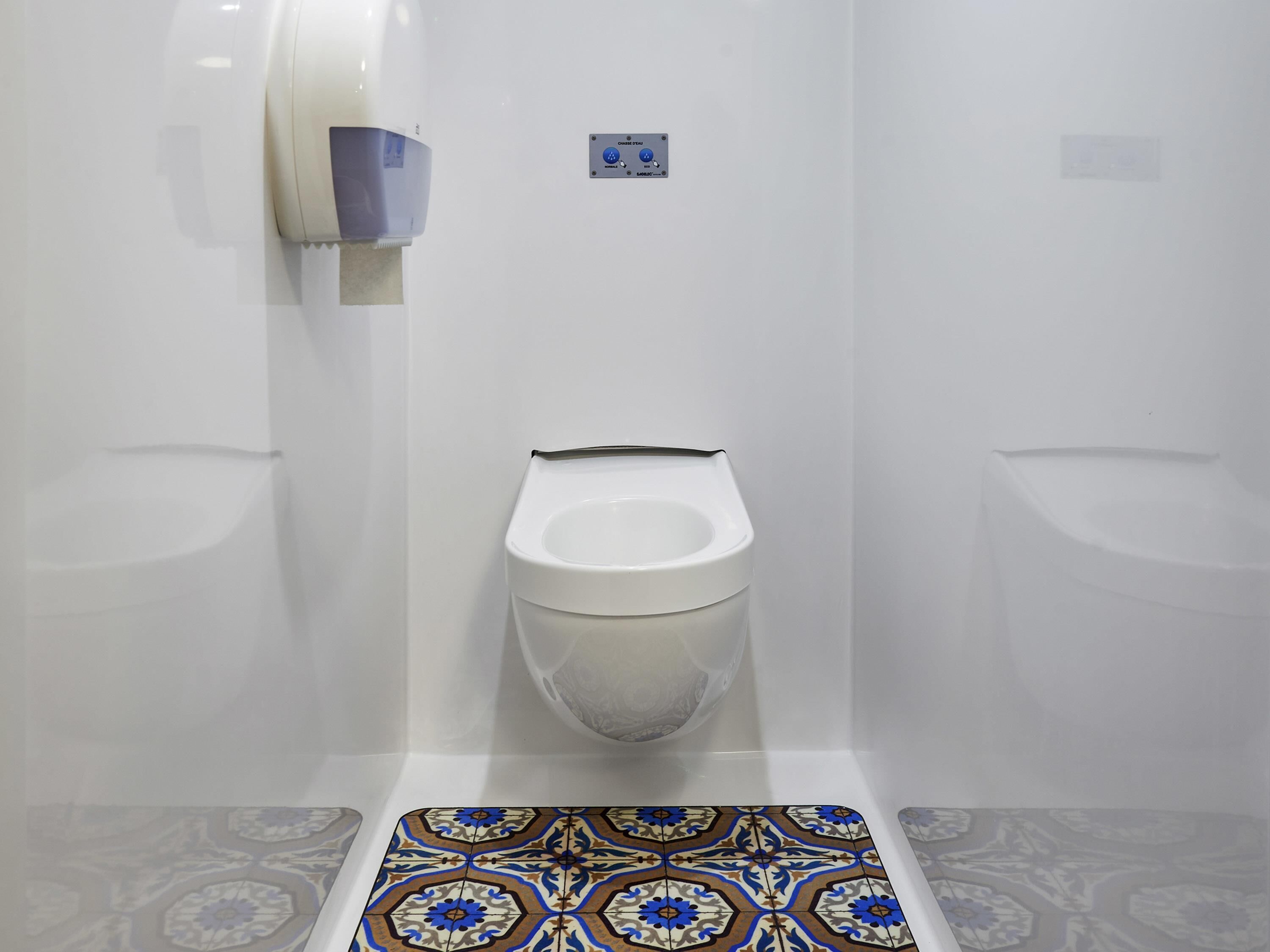 A bathroom with a toilet, a hand dryer, and a wall-mounted flush button.