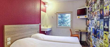 Habitación de hotel con cama, escritorio, televisor y un mural decorado con carteles de viajes.