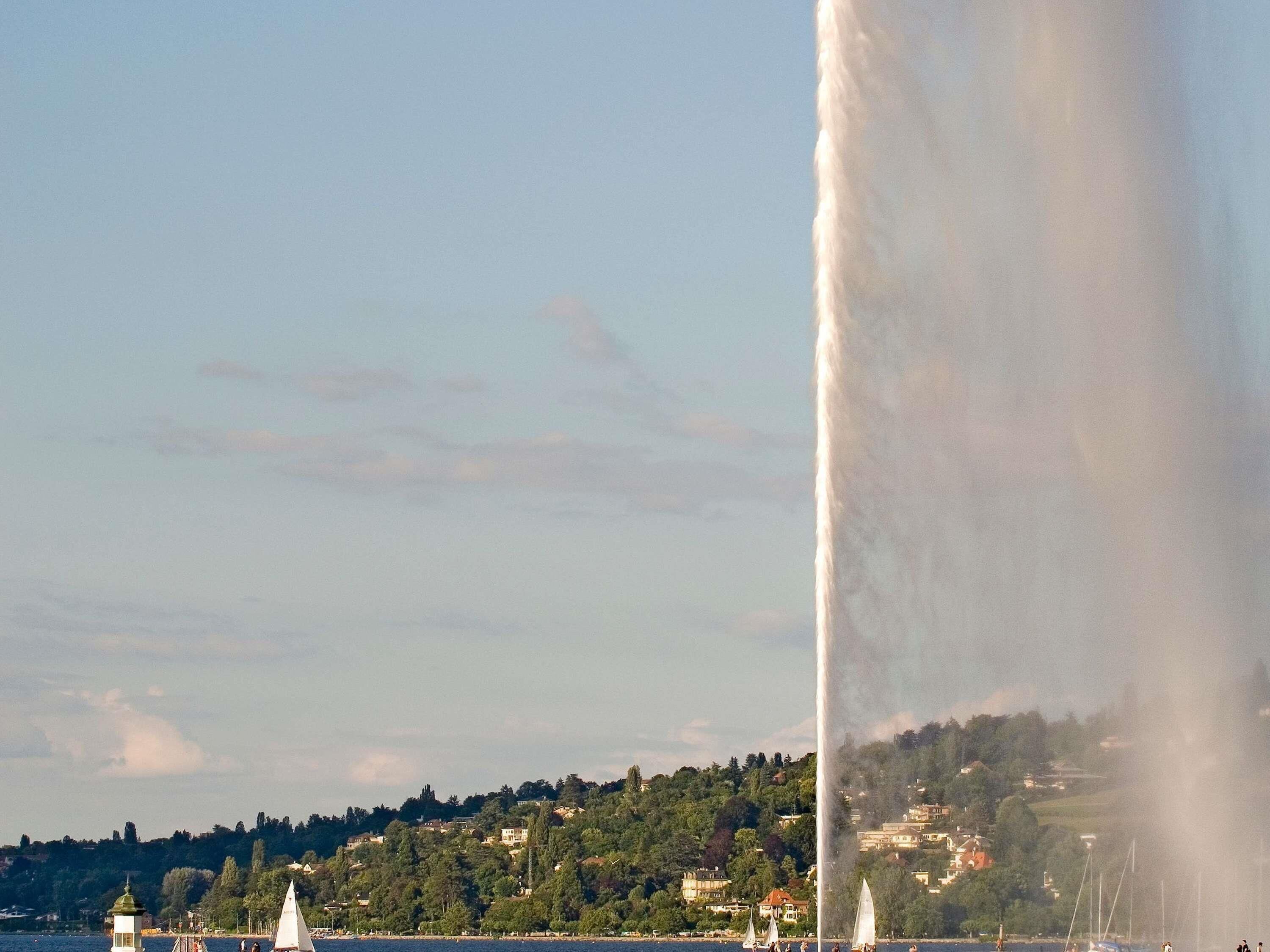 Een fontein met waterstralen, een vuurtoren en een heuvel met gebouwen op de achtergrond.