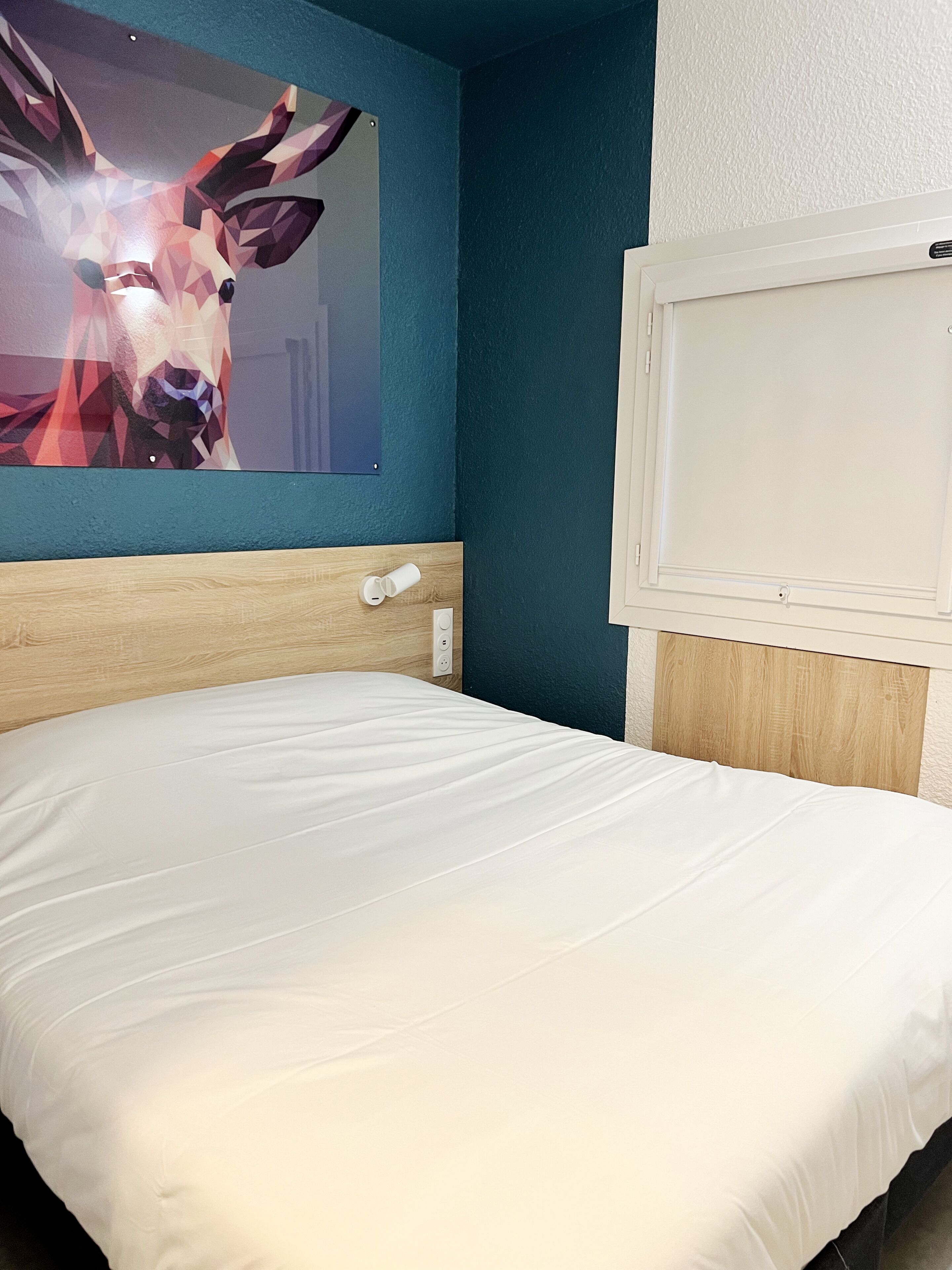 Habitación de hotel con cama, cabecera de madera, interruptor de luz en la pared y un cartel con un ciervo.