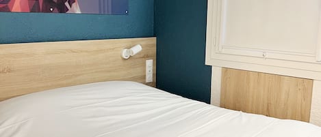 Habitación de hotel con cama, cabecera de madera, interruptor de luz en la pared y un cartel con un ciervo.