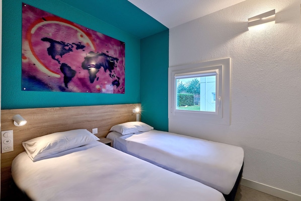Quarto de hotel com duas camas, uma pintura abstrata grande, uma janela com vista para vegetação e um ponto de luz na parede.