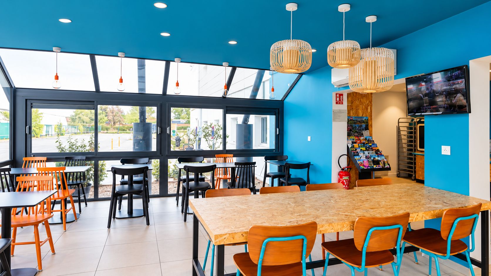 A modern dining area with a large wooden table and chairs, large windows, and hanging light fixtures.