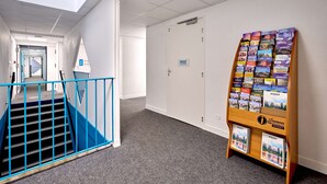 A hallway with a staircase, a door labeled "PRIVÉ," and a display rack with brochures. - Kyriad ECO - Moulins Sud Yzeure (Yzeure)