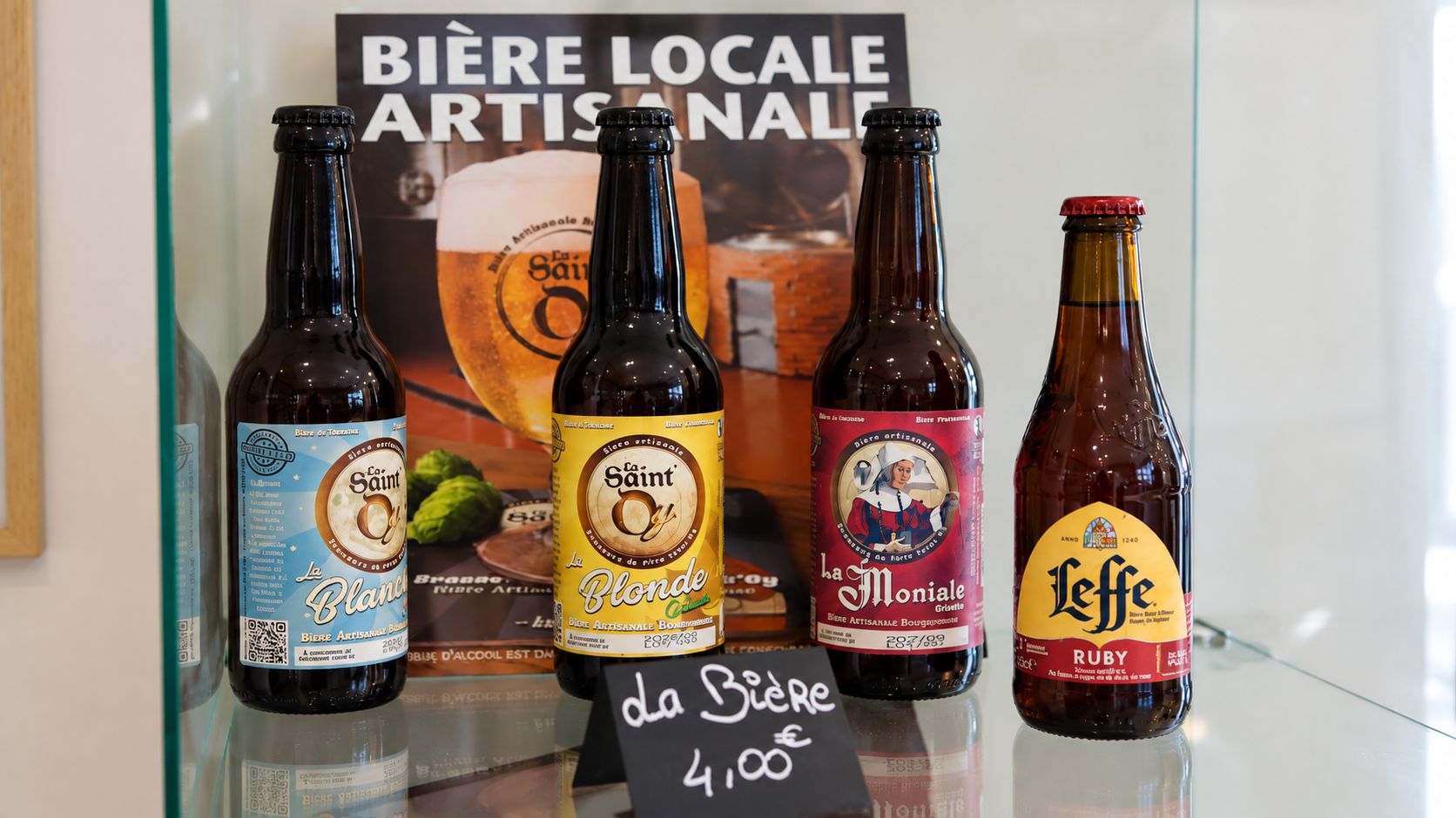 Four bottles of beer with labels, placed on a glass shelf.