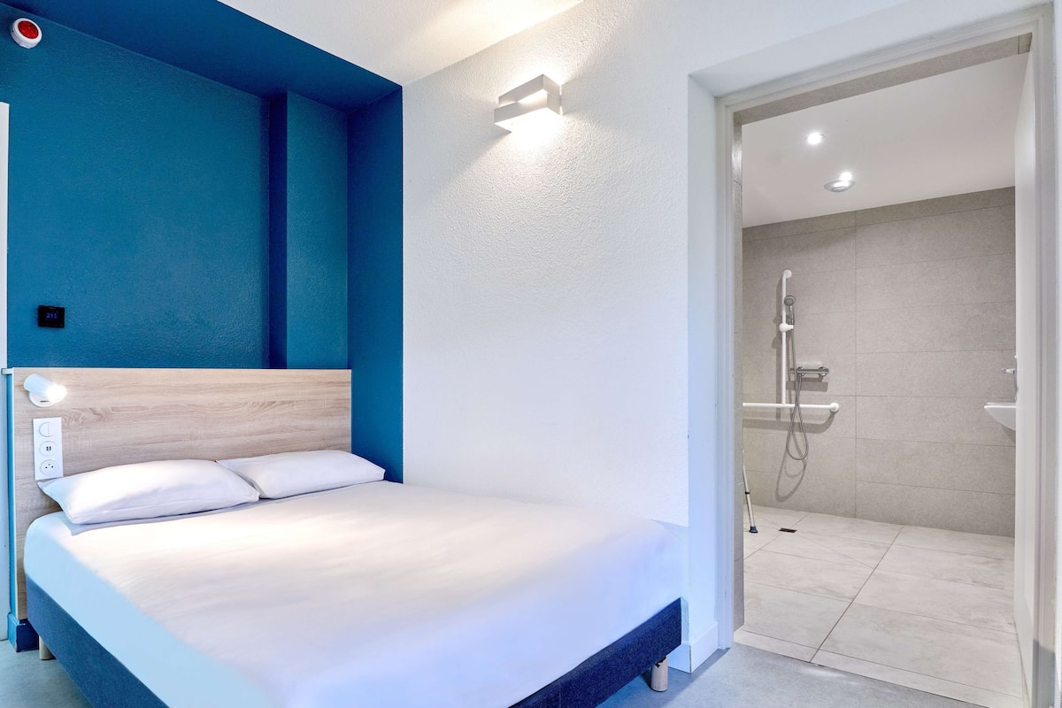 Een moderne hotelkamer met een bed, een douchegedeelte en een blauwe accentmuur.