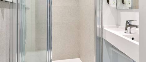 A modern bathroom with a glass-enclosed shower, a white sink, and a mirror above the sink.