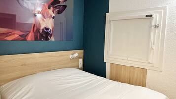 A neatly made bed in a room with a blue accent wall and a framed picture of a deer.