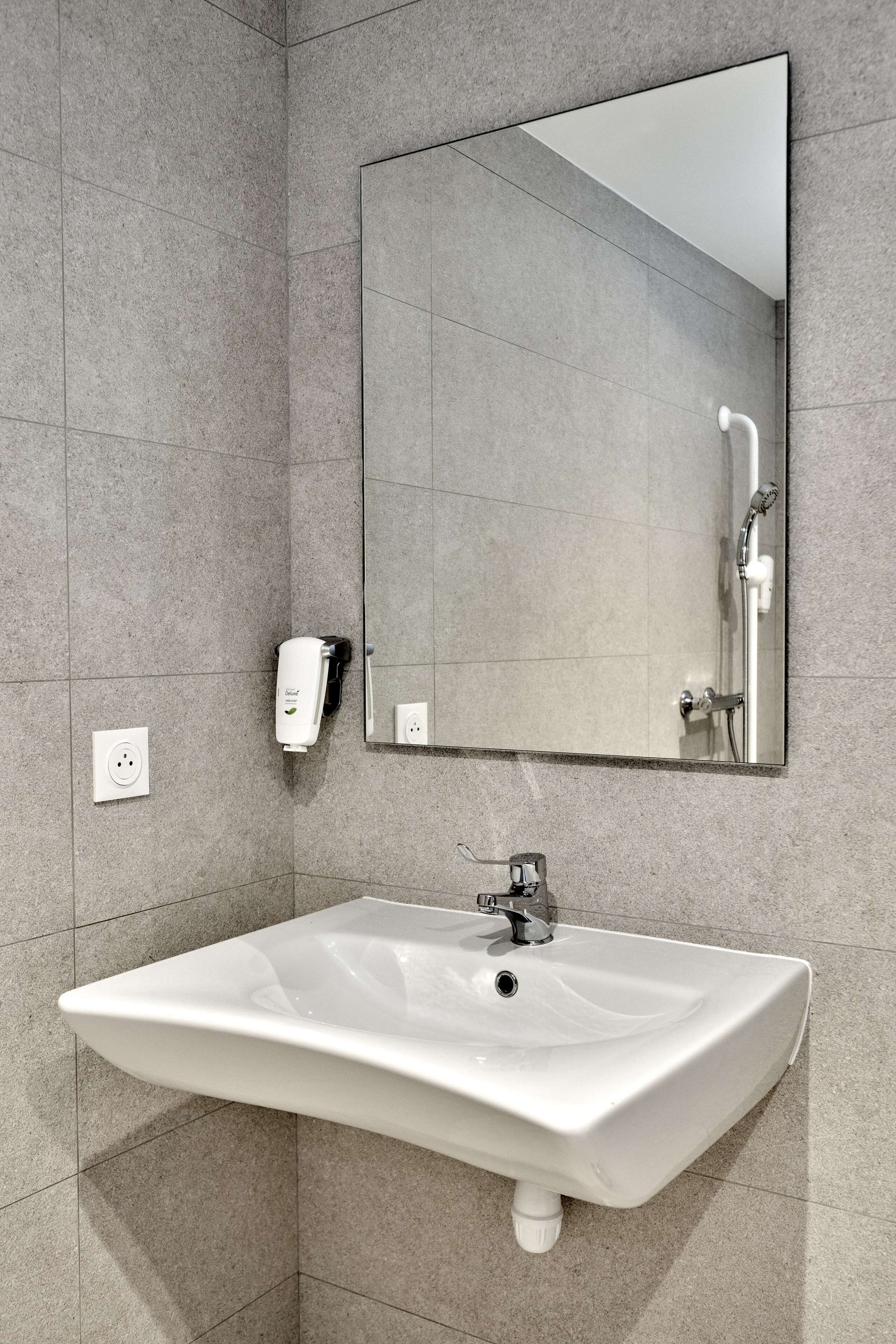 Un baño con lavamanos blanco, un espejo y dispensador de jabón de mano.