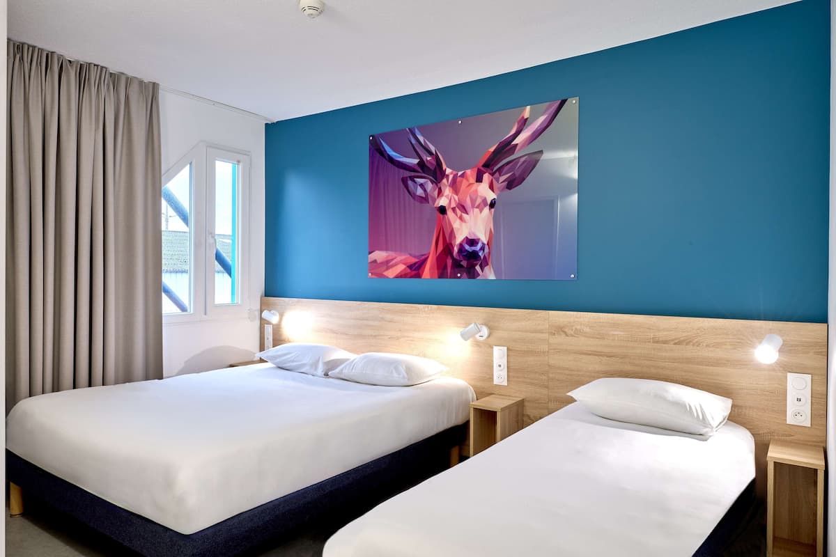Een hotelkamer met twee bedden, een groot wanddecoratie van een hert en een raam met gordijnen.