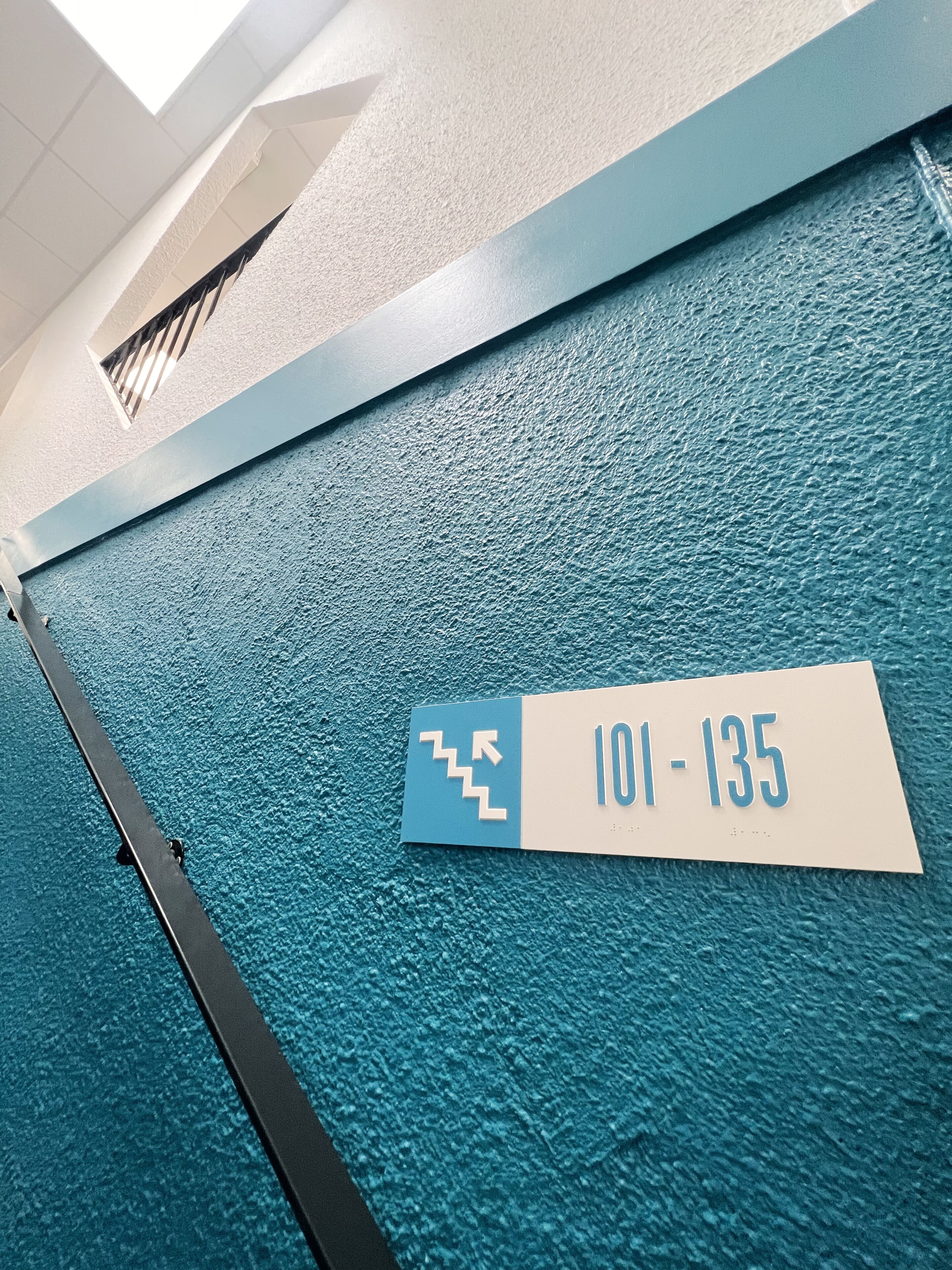 Sininen, kuvioitu seinä, jossa on kyltti, jossa on merkitty huoneiden numerot 101–135.