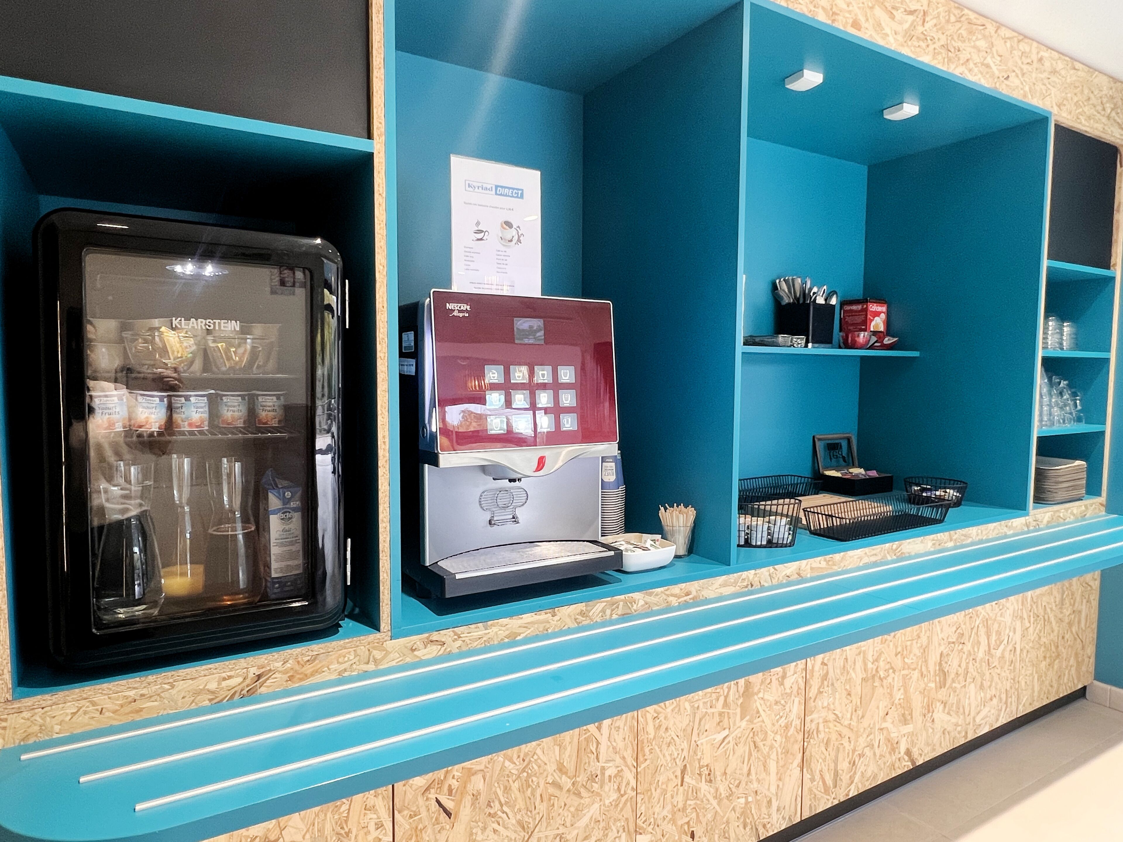 A self-service beverage station with a refrigerator, a coffee machine, and various containers.
