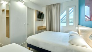A hotel room with a bed, a TV mounted on the wall, a window with curtains, and a view of the outside. - Kyriad ECO - Moulins Sud Yzeure (Yzeure)