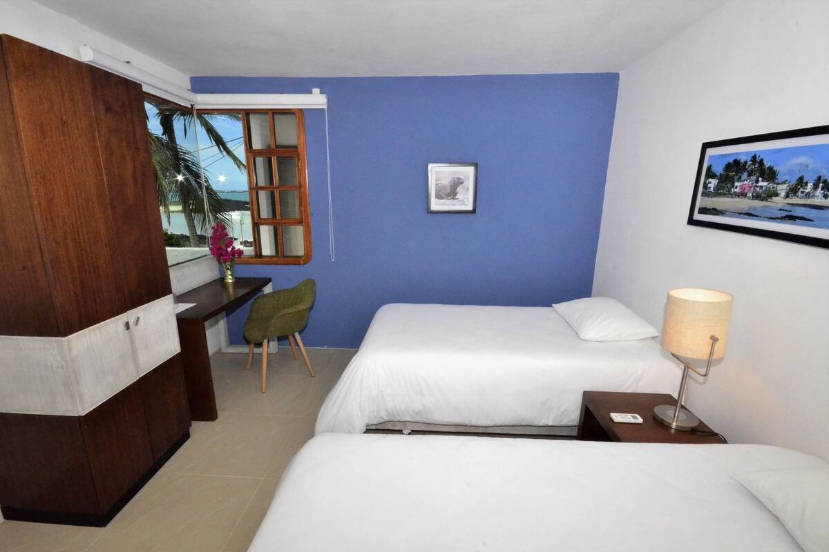 A hotel room with two beds, a desk, a chair, a lamp, and a framed picture on the wall.