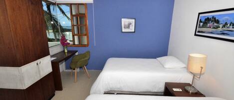 A hotel room with two beds, a desk, a chair, a lamp, and a framed picture on the wall.