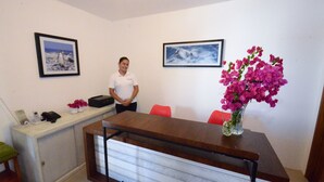 Ein Empfangsbereich mit einem Schreibtisch, Stühlen, gerahmten Bildern an der Wand und einer Blumenvase.