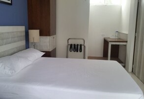 Una habitación de hotel con una cama grande, una mesita de noche, una lámpara, un perchero para toallas y un pequeño baño.