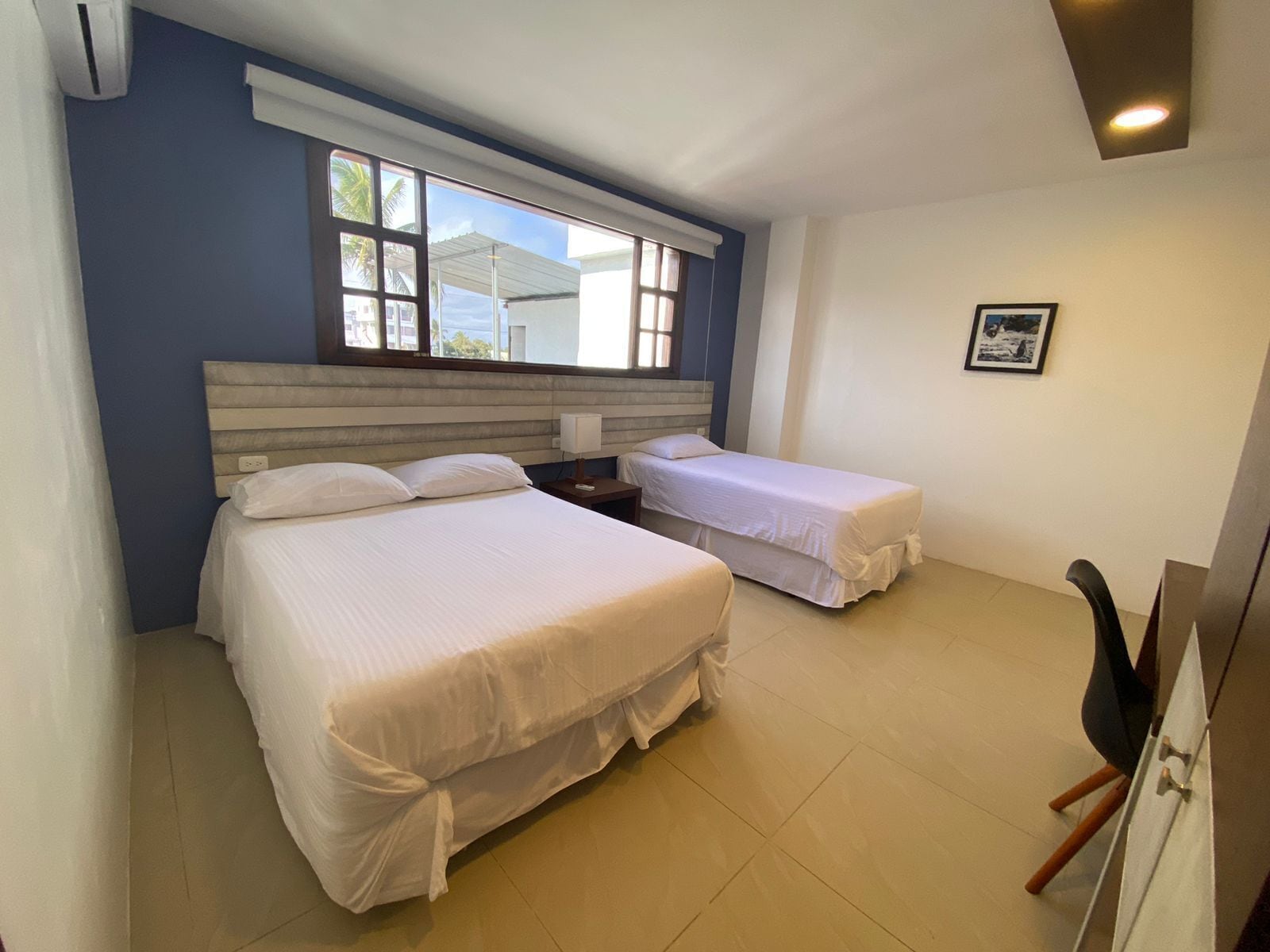 A bedroom with two beds, a window, and a framed picture on the wall.