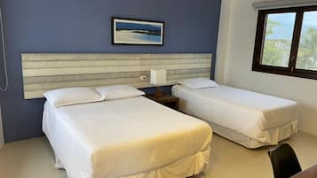 A hotel room with two beds, a headboard, a nightstand, a lamp, and a window with a view of palm trees.