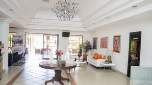 A spacious lobby with a round wooden table, white sofas, and a chandelier. - Farallones Hotel (Chinandega)