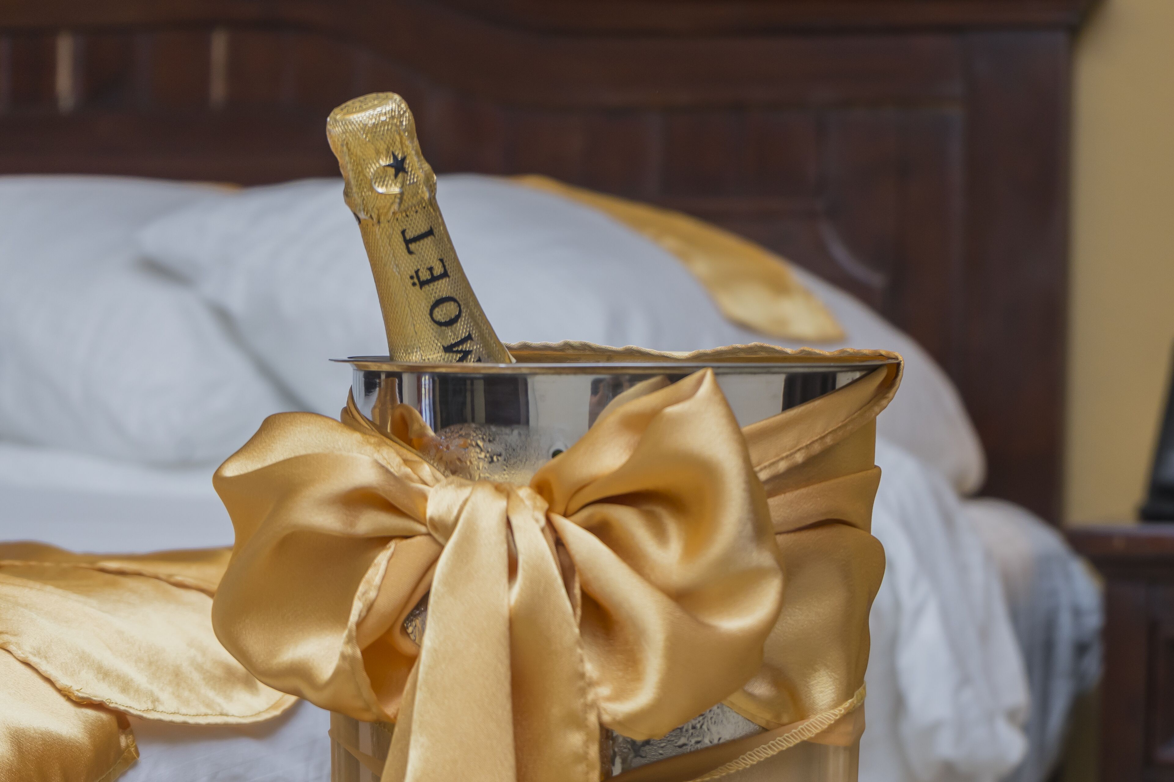Una cama con un recipiente metálico que contiene una botella de champán, atada con un lazo dorado.