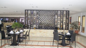 A restaurant with a wine wall, tables, chairs, and a potted plant. - Farallones Hotel (Chinandega)