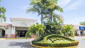 A hotel entrance with a landscaped garden, palm trees, and a clear sky. - Farallones Hotel (Chinandega)