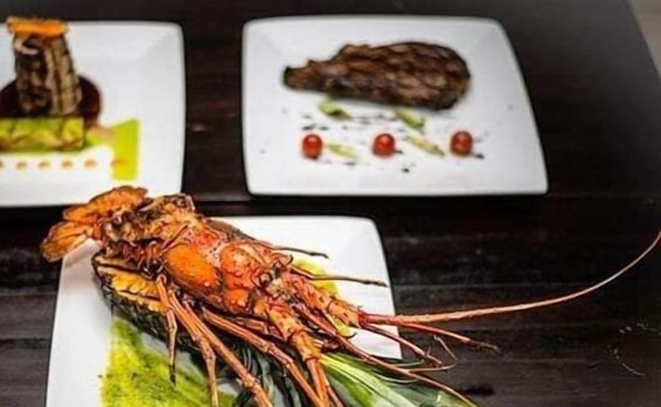 A dining table with three square plates of food, including a lobster and other dishes.