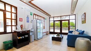A spacious room with a large window, a refrigerator, a sofa, and a trash bin.