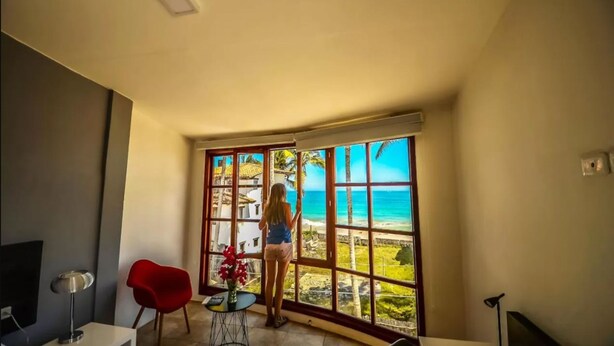A room with a large window offering a view of the beach and palm trees.