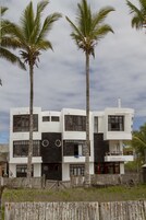 Un edificio moderno de dos pisos con techo plano, ventanas amplias y una cerca de madera al frente.