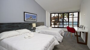 A hotel room with two beds, a desk, a chair, a window with a view of the sea, and a framed picture on the wall.