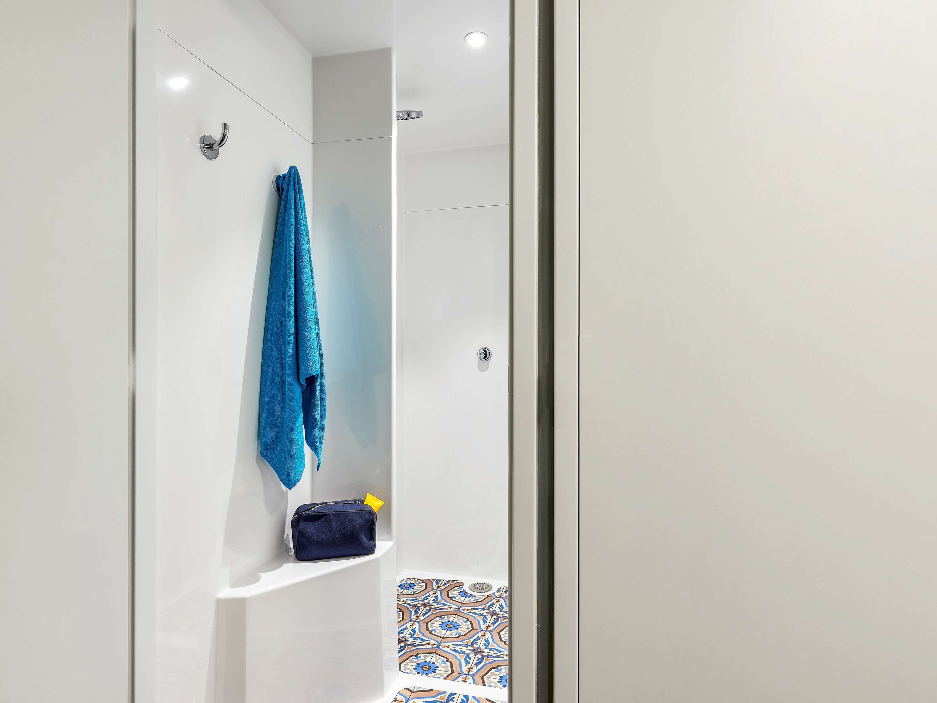 Un baño con ducha, toallero y un pequeño estante con un bolso.