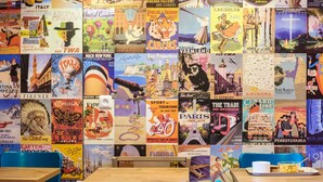 A wall of vintage travel posters with a table and chairs in the foreground.