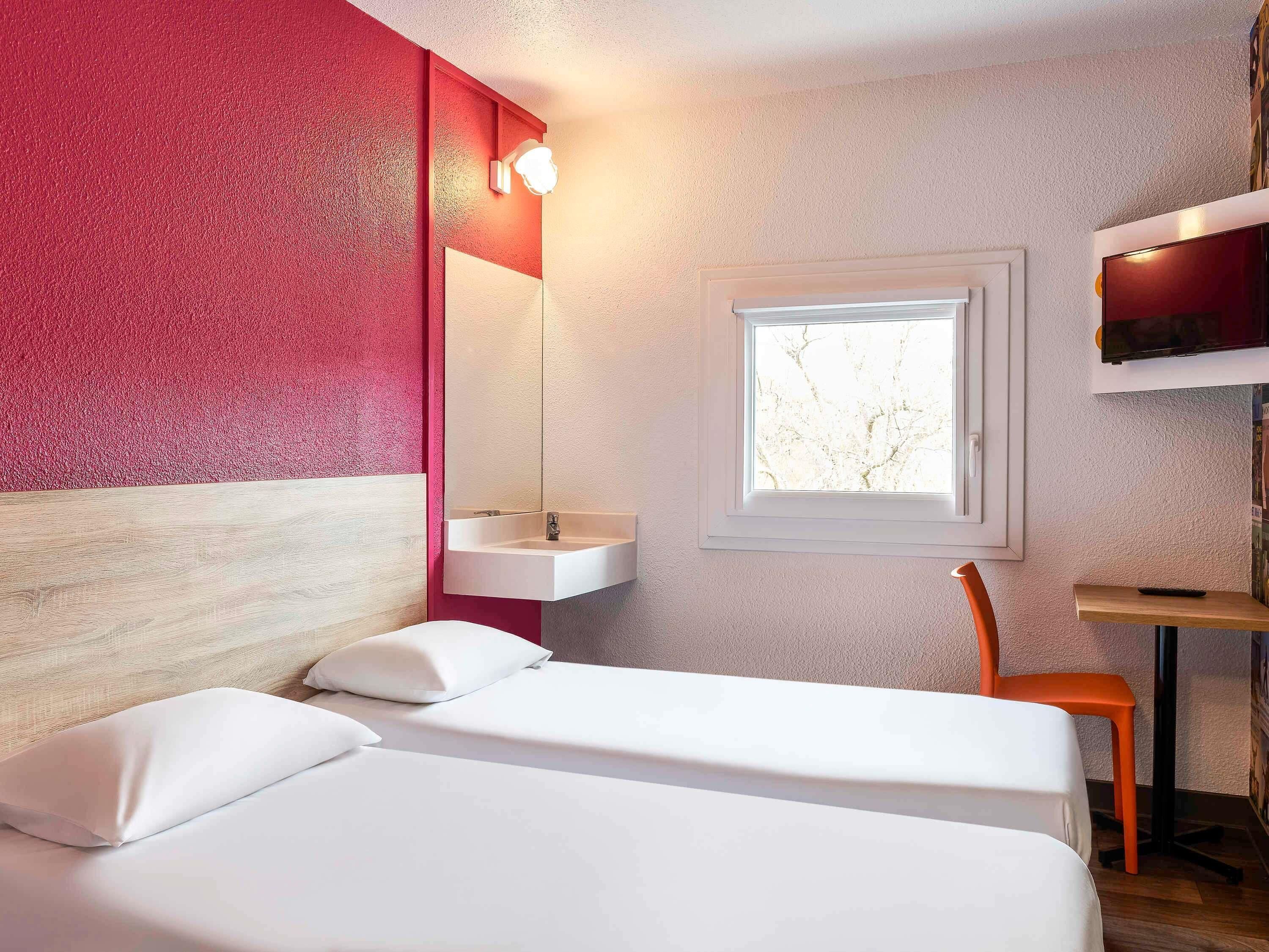 Une chambre d’hôtel avec un lit, une fenêtre, un lavabo et une chaise.