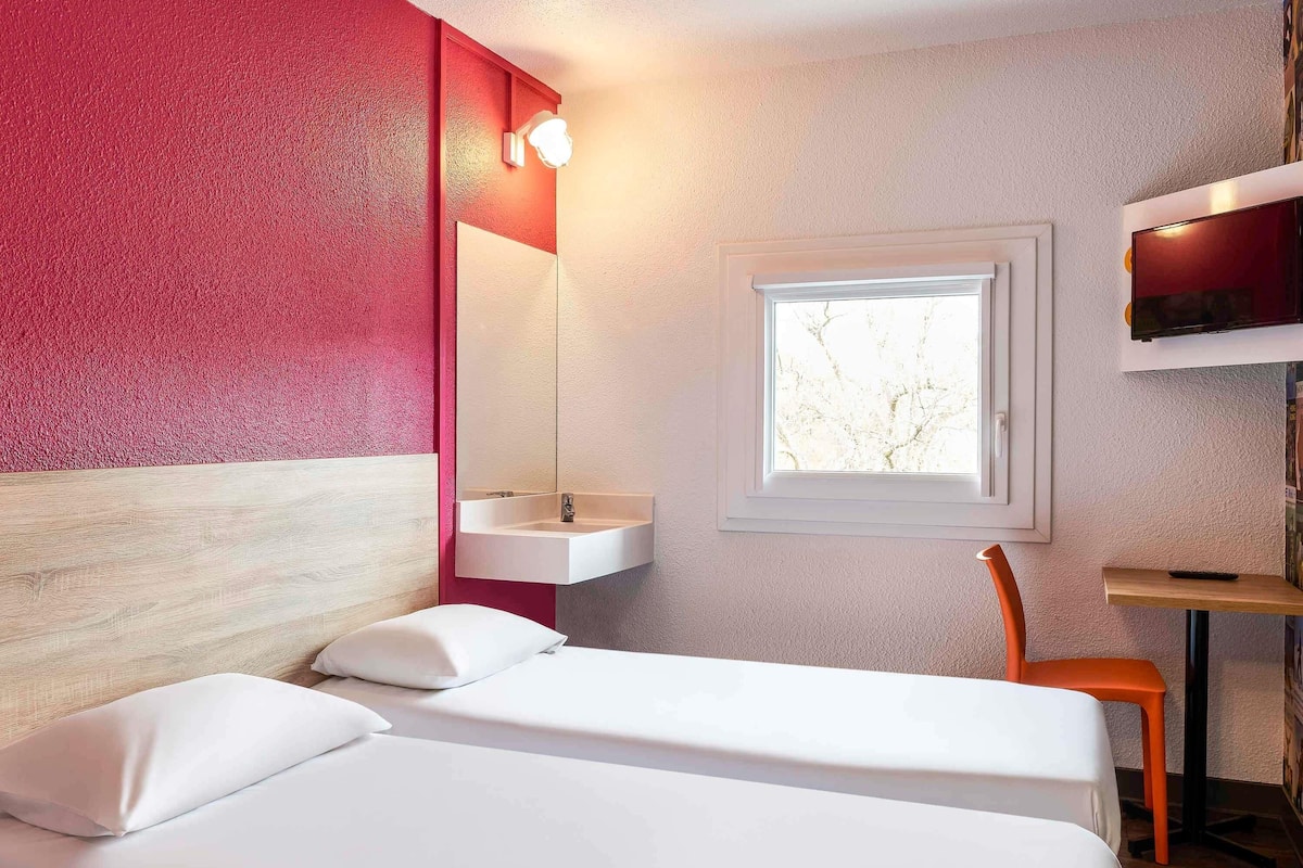 Ein Hotelzimmer mit Bett, Fenster, Waschbecken und Stuhl.