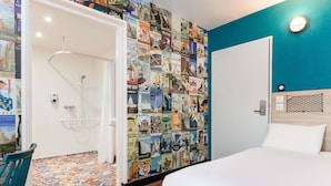 Een hotelkamer met een bed, een douche en een muur vol reisposters.