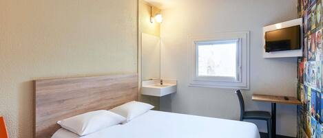 A hotel room with a bed, a desk, a chair, a TV, a window, and a wall with pictures.