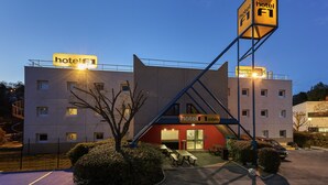 Een hotel met modern design, voorzien van een opvallend bord, een overdekte ingang en terrasplekken.