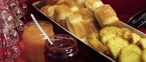 A tray of bread rolls and pastries, a jar of jam, and a glass pitcher.