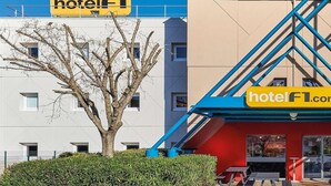 Entrada de un hotel con un letrero azul y amarillo, un toldo rojo y vistas de las ventanas del edificio.