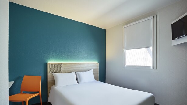 Una habitación de hotel con cama, una silla, un televisor y una ventana con persianas.