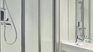Une salle de bain moderne avec une douche à l’italienne en verre, un lavabo blanc et un miroir.