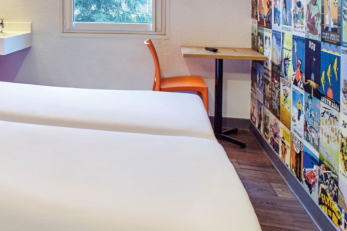 Una habitación de hotel con dos camas, un lavamanos, una silla y una pared decorada con carteles de viajes.