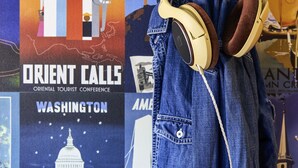 Una chaqueta vaquera con auriculares colgando de una pared con varios carteles de viaje.