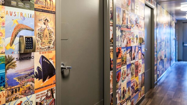 Un pasillo con carteles de viaje en las paredes y una puerta con cerradura electrónica.