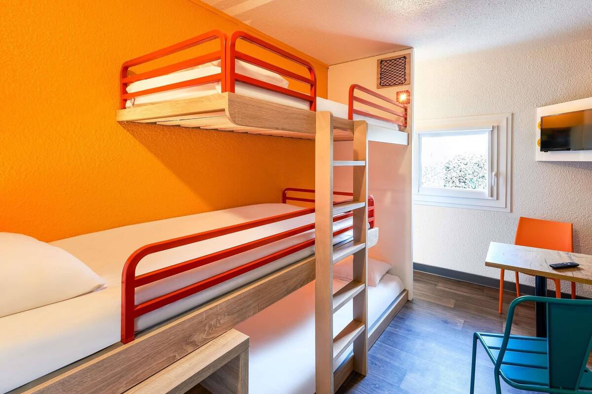 Een slaapkamer met een stapelbed, bureau en stoel, een raam en een televisie.
